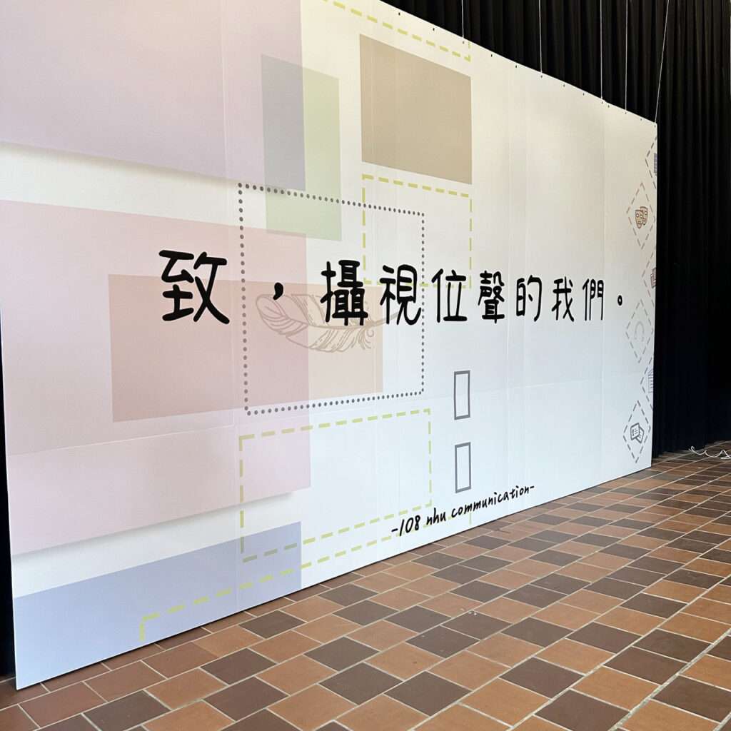 一面大圖輸出，懸掛在布幕前方。上面有致攝視位聲的我們字樣(左側視角)