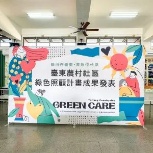 台東農村社區成果發表會快幕秀展架，室內活動現場搭建實景，展示綠色照顧計畫Green Care主視覺與溫馨插畫